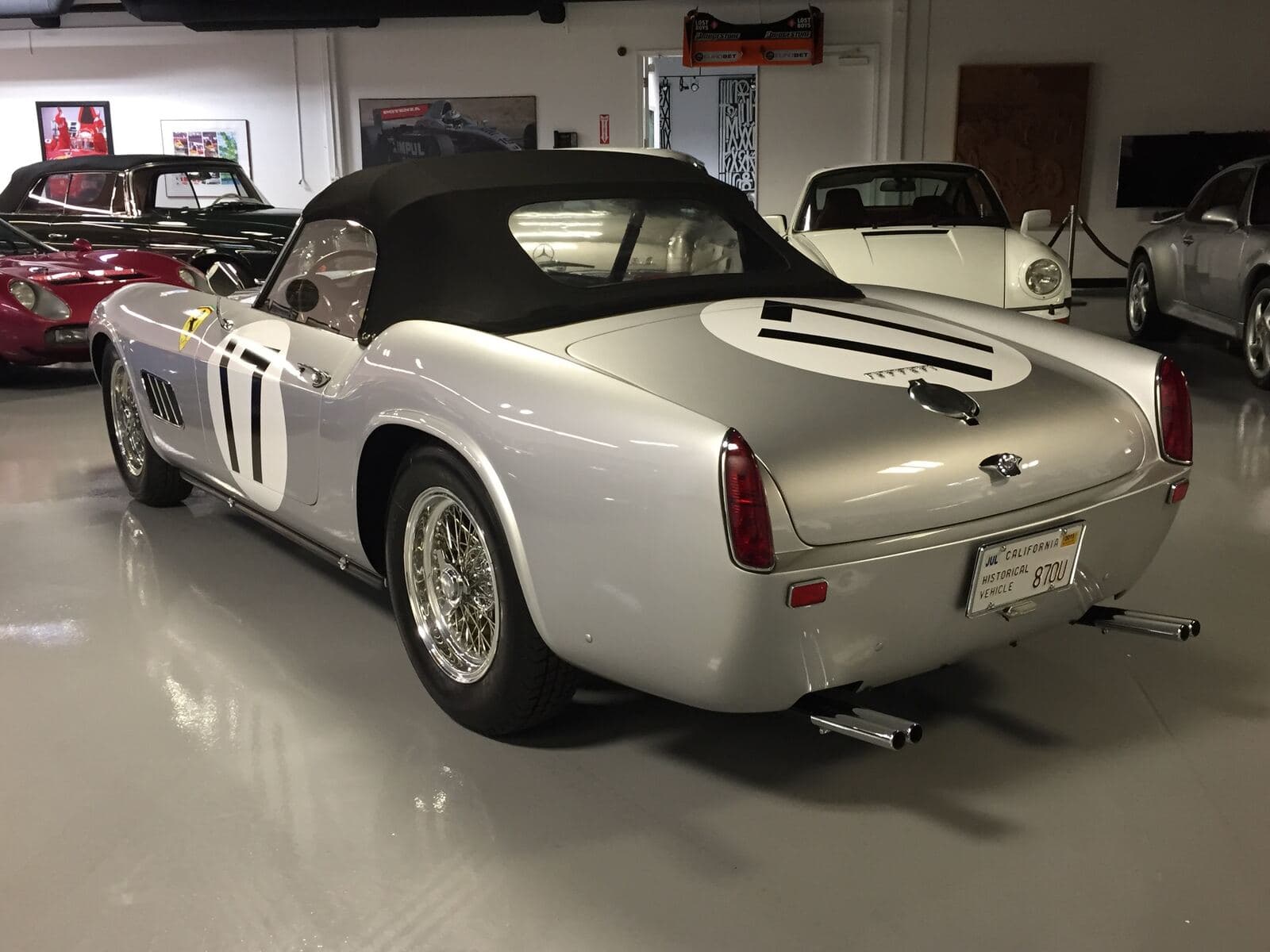 A silver Porsche 356 among cars in a restoration workshop